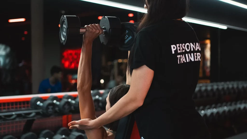 Photo de la coach Inès Coaching accompagnant une sportive pendant un exercice avec haltères en salle, illustrant la technique, la sécurité et l’encadrement personnalisé.